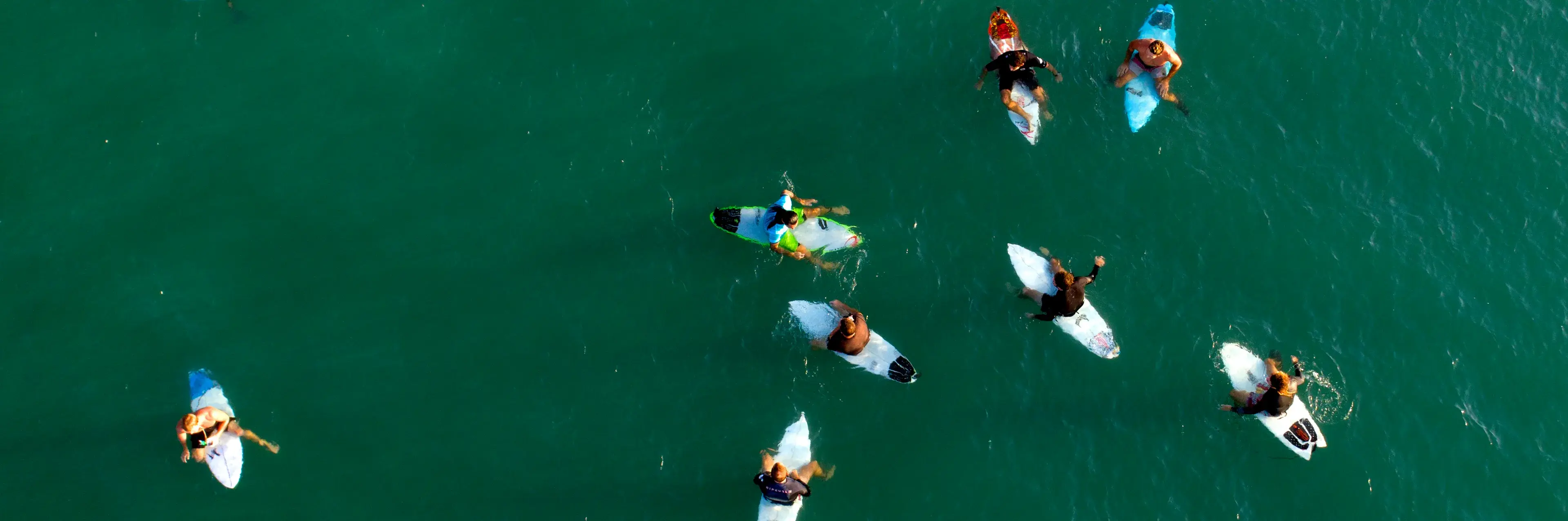 Overhead drone view of surfers sitting and paddling on their boards in green water.
